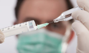 врач набирает вакцину в шприц из ампулы