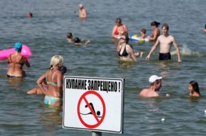 люди плавают на фоне таблички «купание запрещено»