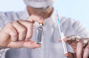врач держит в руках ампулу с вакциной и шприц